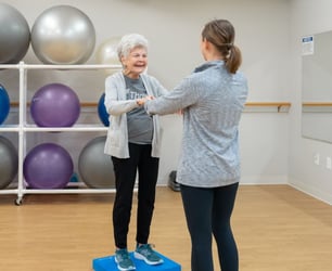 Immanuel instructor supporting elderly woman while exercising.